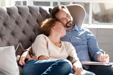Tired of work. Sweet adult couple sleeping on sofa with tablet and notes near big window.