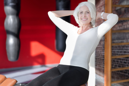 Fitness as lifestyle. Charming senior fit woman smiling and using sports equipment while exercising her abdominal muscles in a gymの写真素材