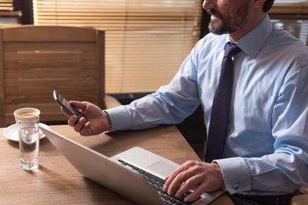 Useful electronic device. Nice handsome bearded man holding a cell phone and looking at its screen...