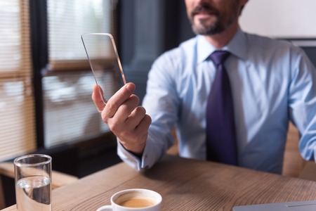 Using modern technology. Selective focus of a modern smartphone being in hands of a handsome male office workerの写真素材