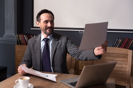 Preparing a presentation. Nice happy confident man holding a sheet of paper and looking at it while preparing to the presentationの写真素材
