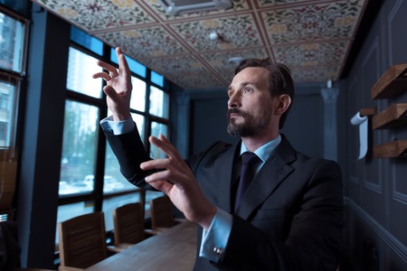 Work with modern technology. Delighted joyful pleasant man looking at the virtual screen and smiling while standing in the conference hallの写真素材