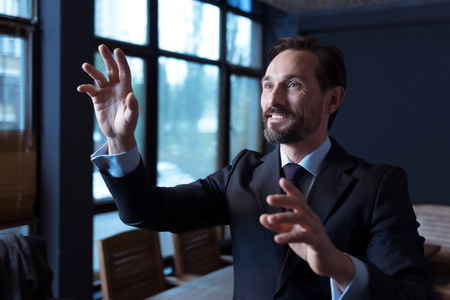 Technological achievements. Positive pleasant good looking man touching an imaginary sensory screen and smiling while standing in the conference roomの写真素材