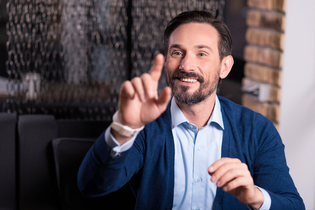 Positive entertainment. Happy optimistic nice man smiling and pressing his finger to the virtual screen while having fun in virtual realityの写真素材