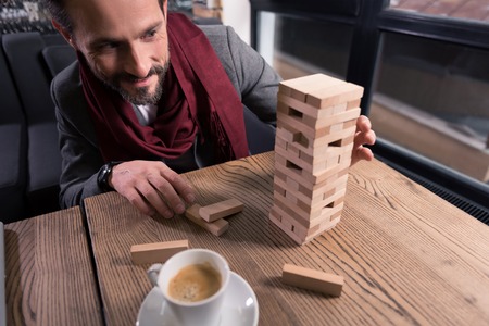 Board games. Joyful nice amused man playing blocks and having fun while relaxing after workの写真素材