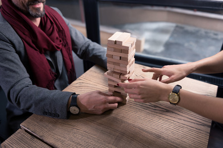Playing the board game. Close up of a blocks tower standing in the middle of the table while being built by happy nice pleasant peopleの写真素材