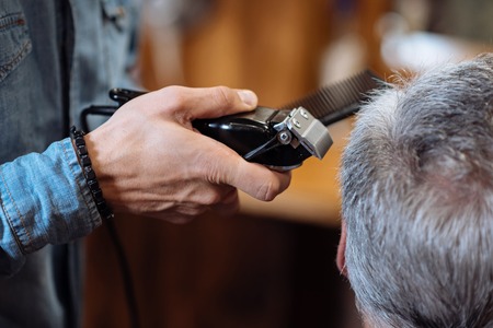Little bit on sides. Back view of senior grey-haired man being trimmed by hairstylist at barbershop.の写真素材