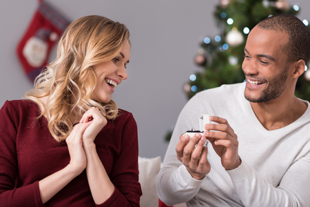 Deliriously happy. Joyful attractive young woman looking at the ring and smiling while receiving a present from her boyfriendの写真素材