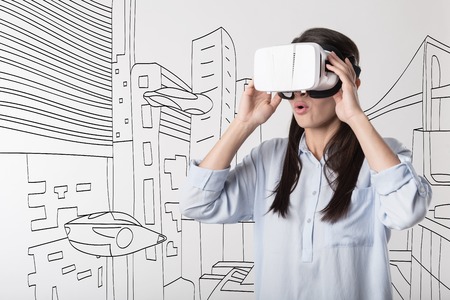 Look at it. Young pretty joyful woman using visual reality device while entertaining and feeling surprise.の写真素材