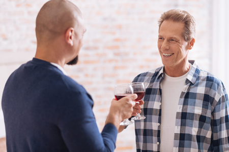 We drinking wine . Smiling involved cheerful non-traditional couple standing in the bedroom and drinking wine while expressing happiness and having conversationの写真素材
