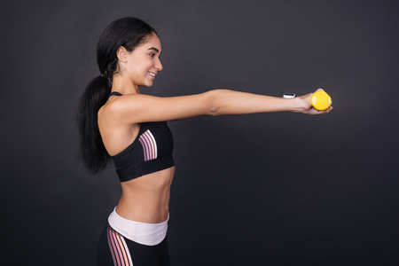 Fitness is my hobby. Healthy young sportswoman standing sideways wearing tracksuit holding both hands in front of herself, isolated on black backgroundの写真素材