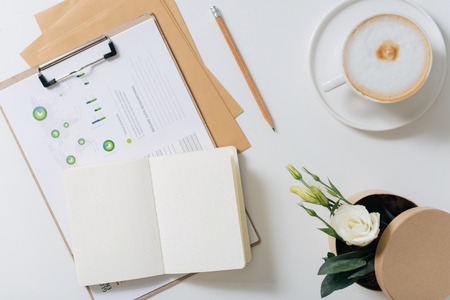 For making notes. Open notebook lying on some diagrams near a cup of coffee and flowersの写真素材