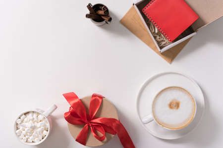 Pleasant surprise. Small round gift box tied with red ribbon standing on the white desk between marshmallows and the cup of coffeeの写真素材