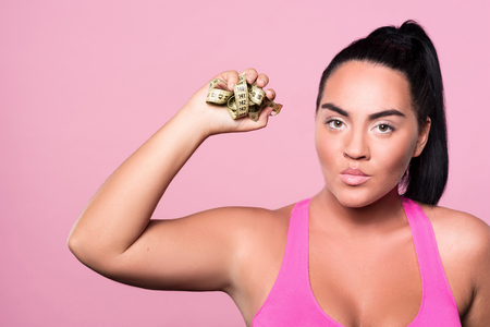 Im fed up. Close up of angry mulatto girl standing against isolated pink wall and holding crumpled body measuring tape.の写真素材