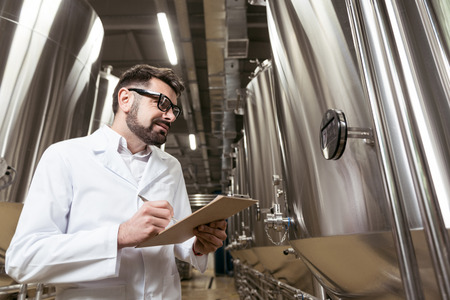 Smiling man making notes in breweryの写真素材