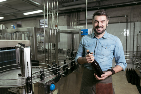 Smiling man holding a bottle of alcohol at brewing factoryの写真素材