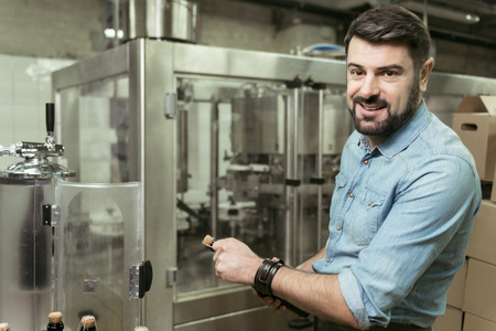 Delighted man opening a bottle of alcohol in brewery