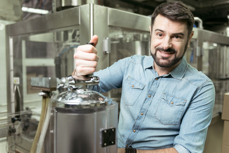 Delighted man pouring alcohol in breweryの写真素材