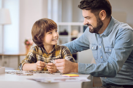 I am happy. Positive bearded male wearing jeans shirt holding puzzle looking at his sonの写真素材