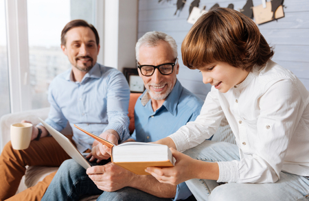 Cheerful positive child showing the book to his grandfatherの写真素材