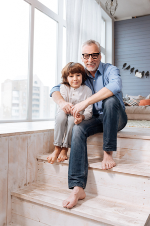 Pleasant delighted grandfather and grandson sitting on the stairsの写真素材