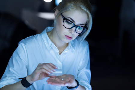 Young businesswoman taking pills at workの写真素材