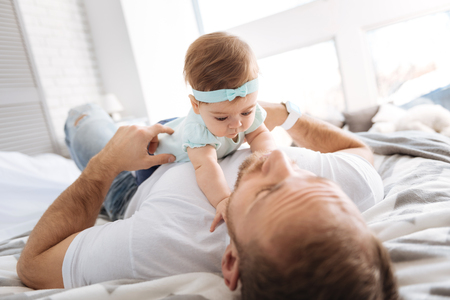 Pretty toddler girl playing games with her parent in the bedroomの写真素材