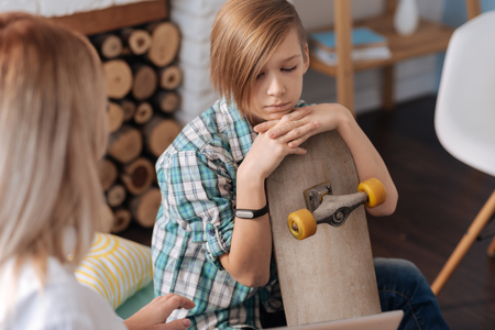 Upset young male person putting his chin on skateboardの写真素材