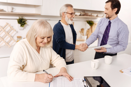 Retired woman signing contract while her husband greeting the notaryの写真素材