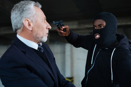 Aggressive greedy robber pointing his gun at the businessmanの写真素材