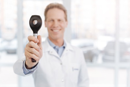 Cheerful medical specialist demonstrating dermatoscope in the clinicの写真素材