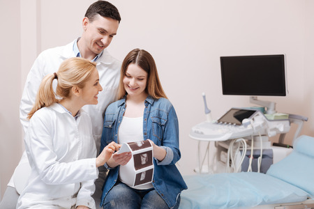 Smiling medics demonstrating ultrasonic results to the pregnant at work