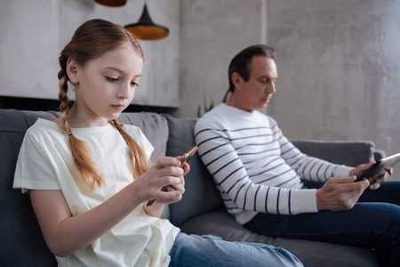 Concentrated granddaughter and grandfather playing digital games indoorsの写真素材