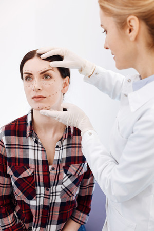 Delighted cosmetic surgeon holding her patients faceの写真素材