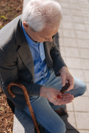 Elderly man taking medicine in the parkの写真素材