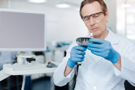Serious lab assistant looking attentively at test glassの写真素材