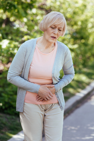 Sad senior woman having pain in the stomach outdoorsの写真素材