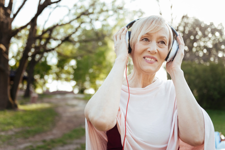 Cheerful aging woman enjoying music in headphones outdoorsの写真素材
