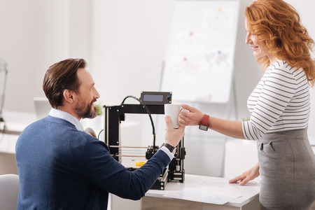 Delighted friendly woman giving her colleague a cup of coffee