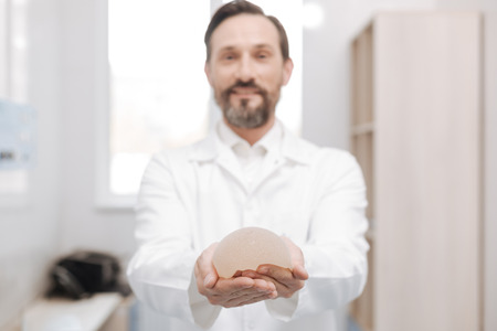 Charismatic competent surgeon holding a breast implantの写真素材