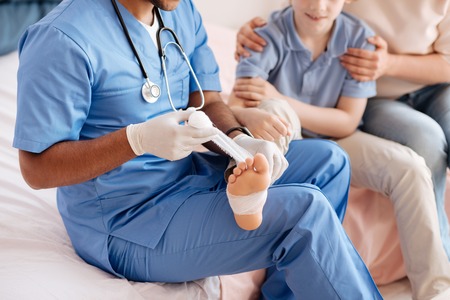 Joyful boy giving his foot for dressing bandageの写真素材