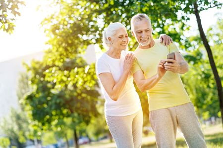 Joyful retired couple using smartphone in the parkの写真素材