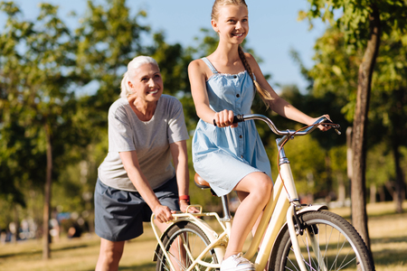 Positive senior woman teaching her granddaughter riding a bicycleの写真素材