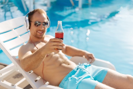 Pleasant man raising a bottle of fizzy drink while sunbathingの写真素材