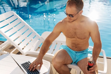Tanned man browsing the Internet near pool