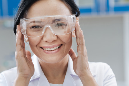 Delighted laboratory scientist fixing her protective glassesの写真素材