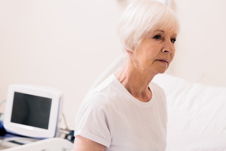 Charming vulnerable aged woman sitting up in hospital bedの写真素材