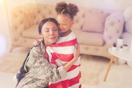 Female soldier hugging her daughter wrapped in American flagの写真素材