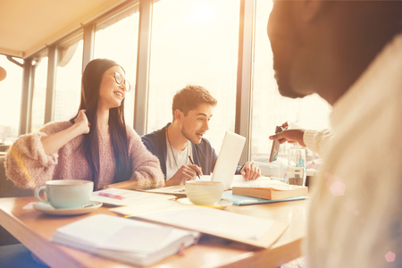 Pleasant afro american student sitting at the table with groupmatesの写真素材
