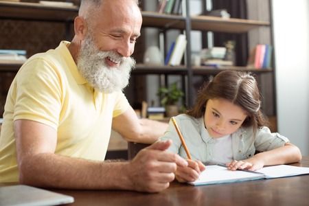 Smiling grandfather helping his granddaughter with homeworkの写真素材